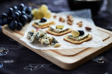 Three blue cheese crackers with grapes are on a cutting board.