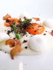 Starter cooked with soft boiled yellow eggs, asparagus, salted meringue and Cretan pork with truffles on top of the dish, served in white plate.