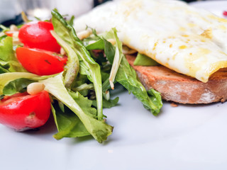 White omelet served with avocado slices on grilled bread toast with fresh lettuce and cherry tomatoes for side dishes ready to be eaten