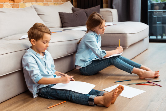 cute siblings sitting on floor and drawing in living room