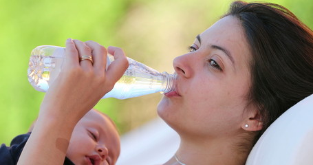 Mother drinking bottle of water while holding sleeping baby