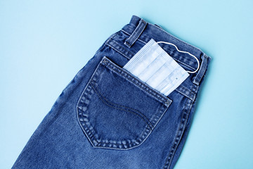 Classic blue jeans on the blue background. Medical mask in the pocket. Pandemic concept. Copy space. Place for text and design. Top view. Flat layout