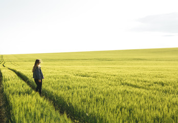 Fototapeta na wymiar Young blonde girl running through the green wheat field. Concept of travel, inspiration, freedom, lifestyle.