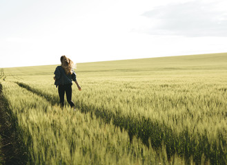  Young blonde girl running through the green wheat field. Concept of travel, inspiration, freedom, lifestyle.
