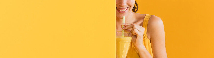 Woman in yellow dress with a glass of juice. Colorful creative yellow studio background.