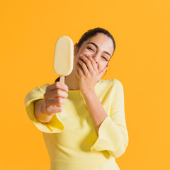 Happy woman with ice cream laughing covering mouth. Colorful creative yellow studio background.