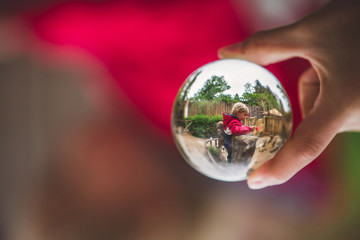 Little child holding poppy in a garden, picture taken through a glass ball