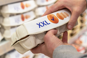 Man chooses and checking quality packing of xxl size eggs in the supermarket. Shopper in grocery...