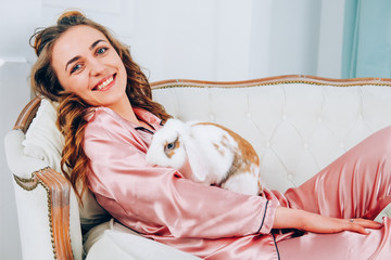 Cute smiley woman in pajamas holding pet rabbit