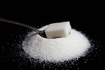 Sugar cube on a spoon. Spoon on a pile of sugar. Photo on a black background