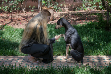 Beautiful Moroccan Arab muslim woman with long blond hair is training obedience with a young black Sloughi dog (Arabian greyhound), inside a backyard garden.