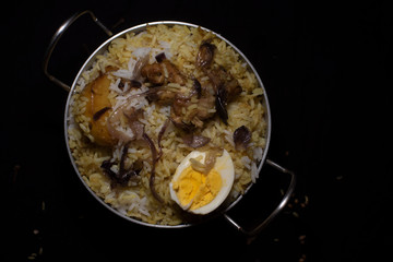 Top down image of Indian spicy dish Biryani with egg, potato and Chicken in a pot in dark copy space background. Food and object photography.