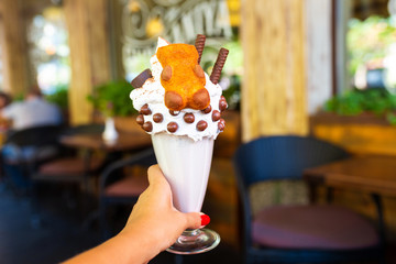 Cool milkshake with cookies and chocolate balls. Milkshake in a glass beaker on a table on a street platform in a cafe. Refreshing summer drinks