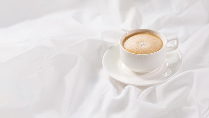 Cup of coffee in bed on a white sheet. Cappuccino and morning routine. Copy space. Concept minimalism