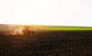 Farmer with tractor seeding sowing crops at agricultural fields in spring at sunset 