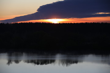 Fototapeta na wymiar Dramatic sky background.The Golden light of the rising sun at dusk illuminates the overhanging continuous cloud on the clear horizon and the forest reflected in the ripples of a calm lake.Russia