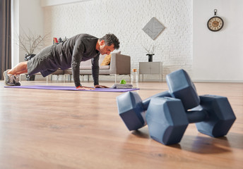 Strong sportive man doing exercises at home, close up dumbbell, sport mat, decorative background living room concept.