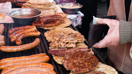The old man's hands are holding a wallet with 500 Serbian dinars while buying grilled meat.