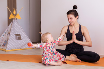 mother practices yoga at home with her child. Sport of a young mom with a toddler. Daughter...