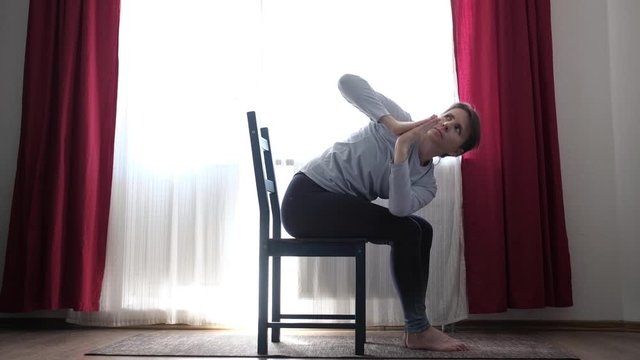 Young fit woman practicing yoga exercise called Twisted Chair Pose or Parivrtta Utkatasana