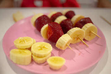 Mixed banana and strawberry pieces on a stick served on a pink plate
