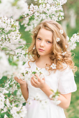 Beautiful thoughtful teen girl in a white dress on a background of flowers in spring