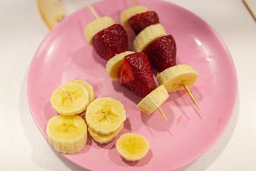 Mixed banana and strawberry pieces on a stick served on a pink plate