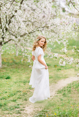Beautiful young girl in a white long dress in a blooming spring garden
