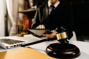 justice and law concept.Male judge in a courtroom with the gavel,working with,digital tablet computer docking keyboard,eyeglasses,on wood table in morning light