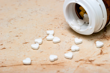 Pills in the shape of a heart on a pink marble background pour out of a jar of medicines.