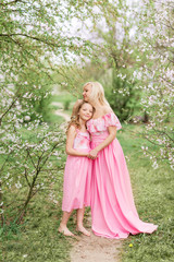 Mother and daughter in pink dresses in a blooming garden in spring.