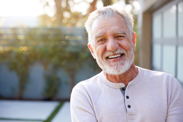 Portrait Of Smiling Retired Senior Hispanic Man In Garden At Home Against Flaring Sun - obrazy, fototapety, plakaty