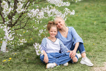 Naklejka na ściany i meble Happy mother and daughter sit on the grass in a blooming garden in spring