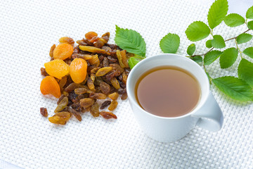 cup of green tea on a white background next to raisins, prunes and dried apricots with green foliage