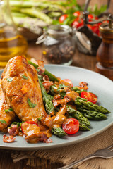 Roasted chicken breast, served on asparagus with tomato sauce, dried tomatoes. Front view.