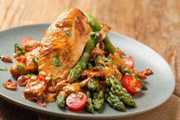 Roasted chicken breast, served on asparagus with tomato sauce, dried tomatoes. Front view.