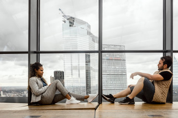 A couple sitting together by huge glass window, but thinking about different things, London, UK