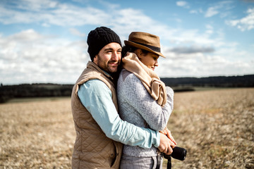 Young couple with camera hugging in the middle of the field.