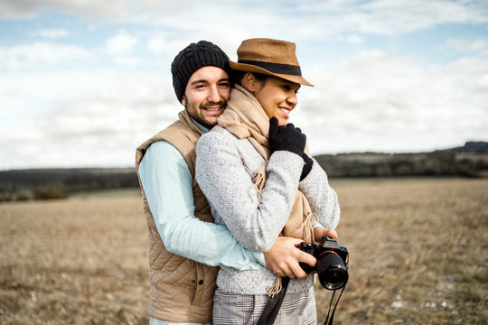 Young couple with camera hugging in the middle of the field.