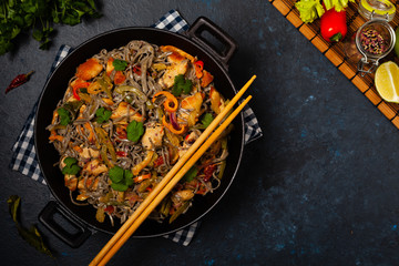 Wheat noodles with black sesame, fried in a wok with chicken and vegetables. Top view.
