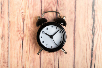 black vintage alarm clock on a wooden table, top view. concept of time, daily routine