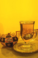 Vertical image of a cup of hot tea with wooden sugar bowl on yellow wall