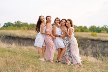 Fototapeta premium A cheerful company of beautiful girls friends enjoy the company and have fun together in a picturesque place of green hills.