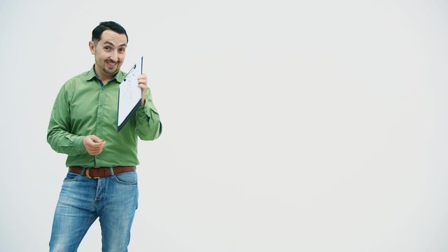 Funny young man standing holding the paper holder with word "bisiness" writen on it, showing it at the camera, pointing at it, playing, moving comically.