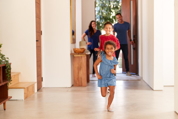 Excited Family Returning Home After Trip Out With Children Running Through Front Door
