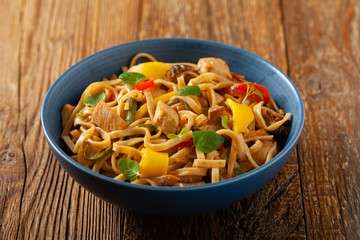 Fried chicken with mango and coconut milk with noodles. Prepared in a wok. Front view. Served in a blue bowl.