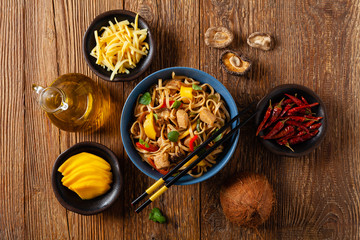 Fried chicken with mango and coconut milk with noodles. Prepared in a wok. Top view.  Served in a blue bowl.
