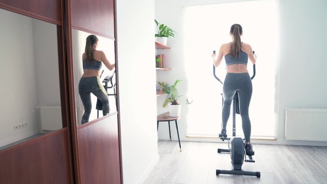 Rear view of young woman on cross trainer at home