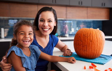 Fototapeta premium Portrait Of Mother And Daughter Carving Halloween Lantern From Pumpkin At Home