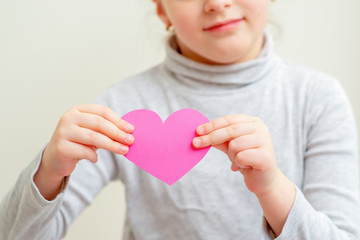 Child is holding pink paper heart standing on white background. Child love concept.